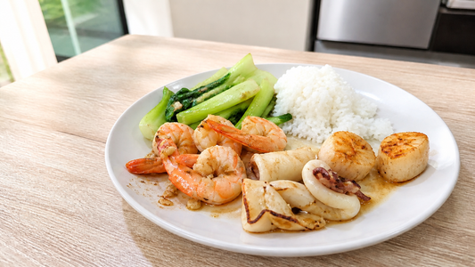 Bright home-cooked prawns, squid, scallops, vegetables, and rice on a ceramic plate
